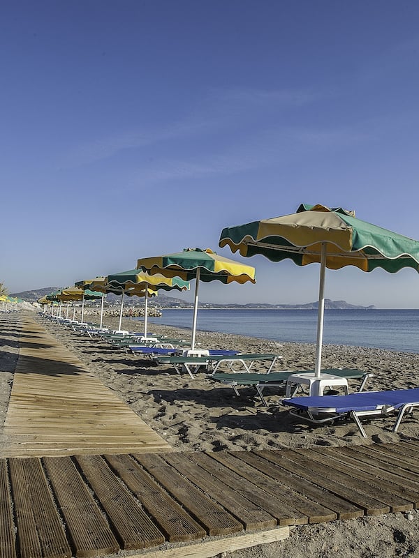 Na praia, areia preta, espreguiçadeiras, guarda-sóis