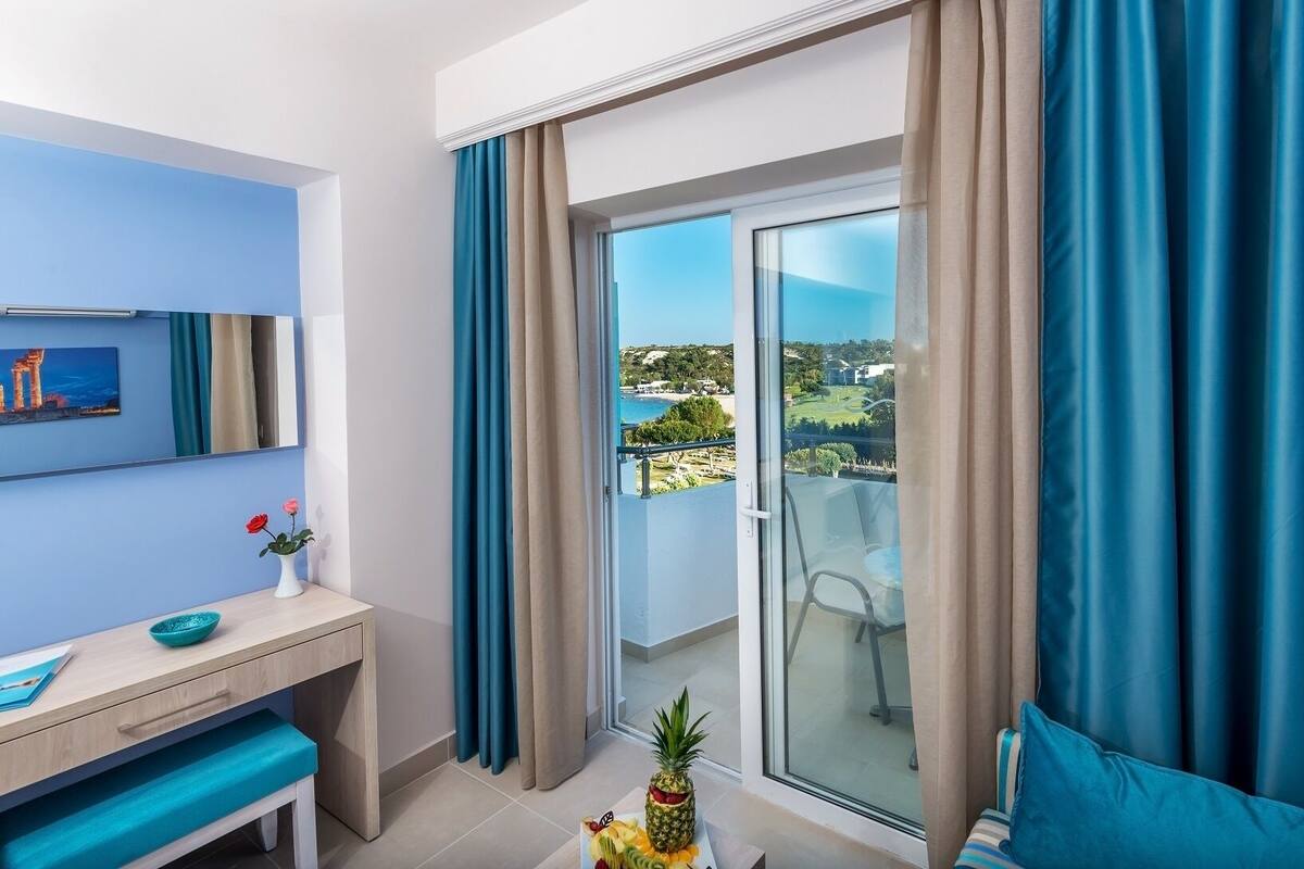 A modern room with a balcony, a desk, a chair, and a view of the sea and landscape.