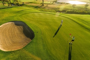 Een golfbaan met een zandbunker, een putting green en een waterhindernis.