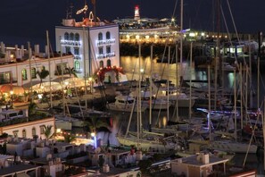 A marina at night with boats docked, a lighthouse in the background, and buildings with lights.