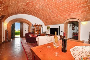A living room with a brick ceiling, a wooden table with wine glasses and a bottle, a red sofa, and a TV. - Antinoro Apartments (Montelupo Fiorentino)