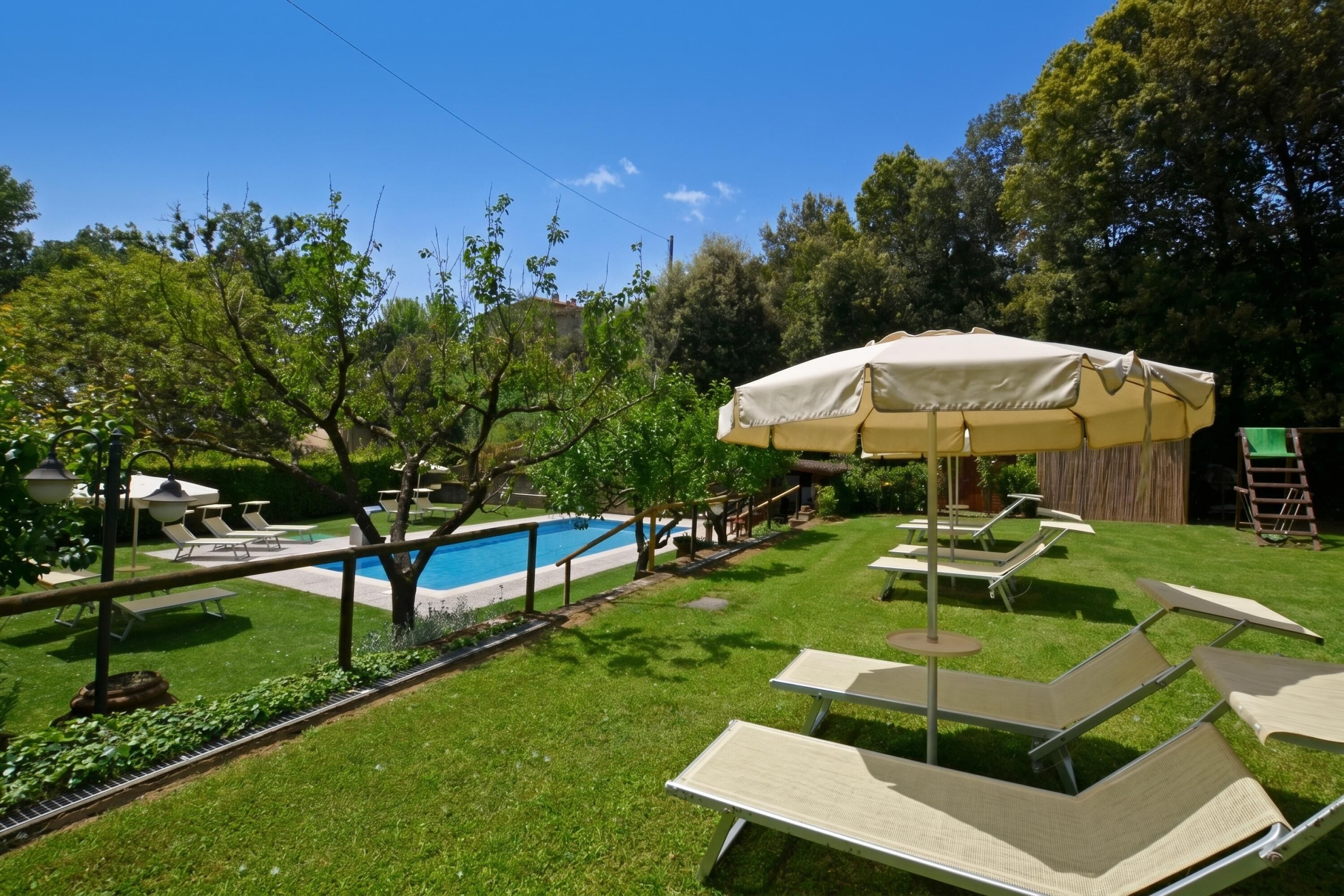 A backyard with a swimming pool, lounge chairs, and an umbrella.