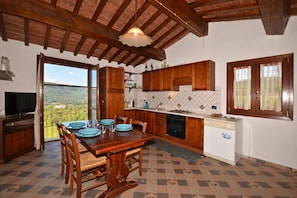 A kitchen with wooden cabinets, a dining table with chairs, a TV, and a view through a large window. - Antinoro Apartments (Montelupo Fiorentino)
