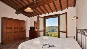 A bedroom with a large bed, a wooden wardrobe, a television, and a view of a landscape through a window. - Antinoro Apartments (Montelupo Fiorentino)