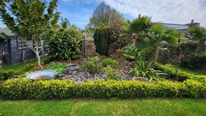 Un jardín cuidado con varias plantas, un pequeño estanque y un muro de piedra.