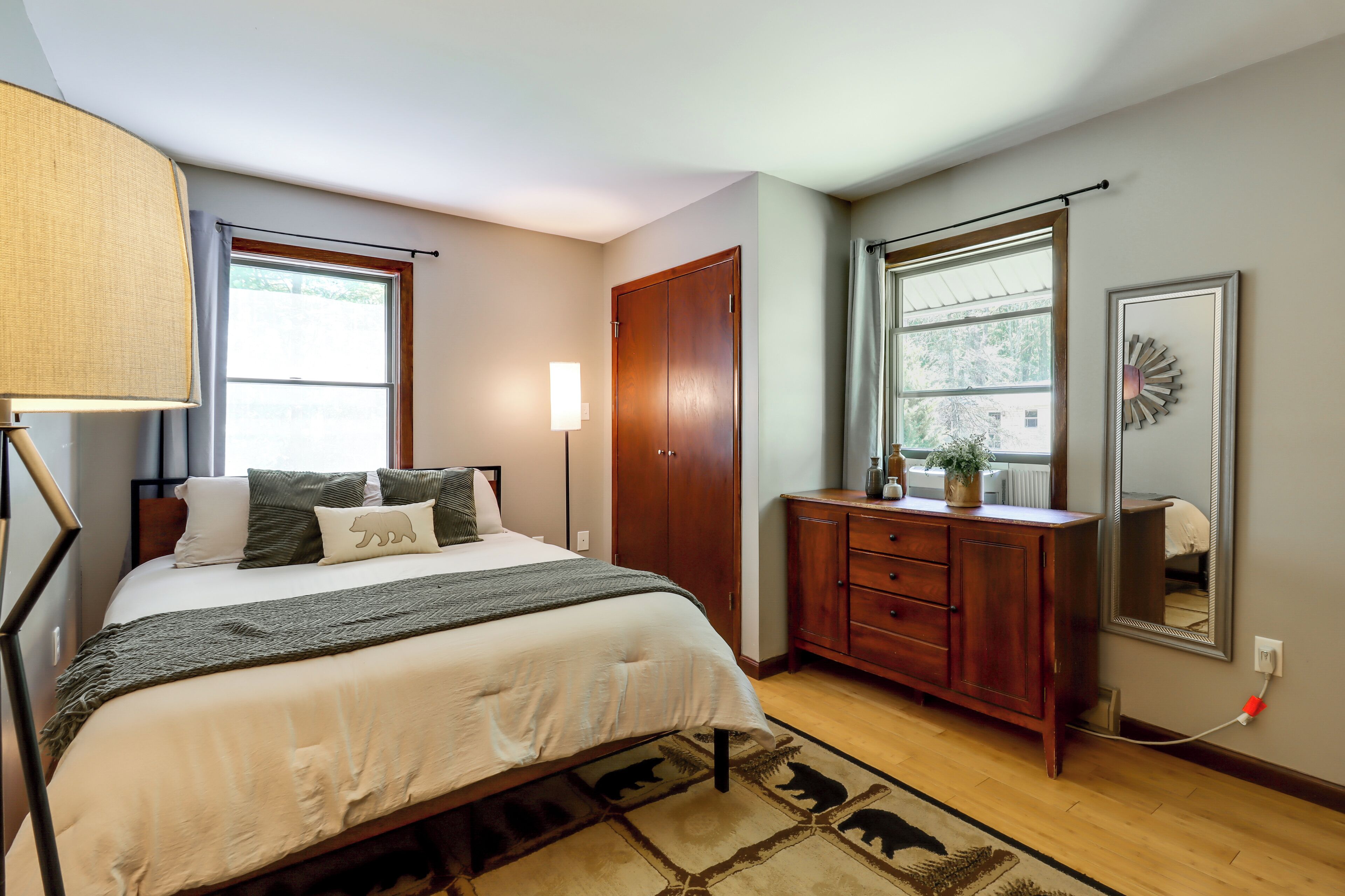 A bedroom with a bed, bedside lamp, wardrobe, dresser, and a mirror.