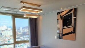A modern living room with a sofa, a coffee table, and a large window offering a city view. - Hotel Kenny Yeosu (Yeosu)