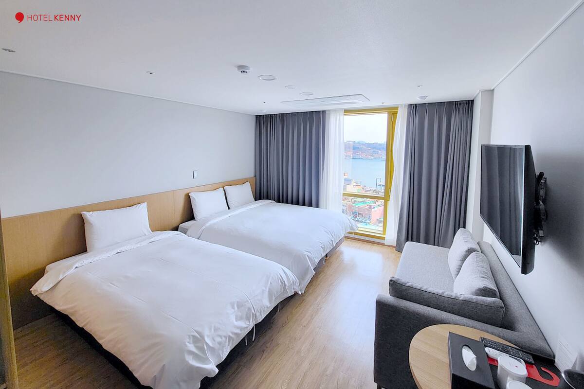 Quarto de hotel com duas camas, um sofá, uma televisão e uma varanda com cortinas.