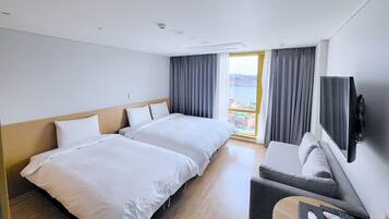 A hotel room with two beds, a sofa, a TV, and a balcony with curtains.