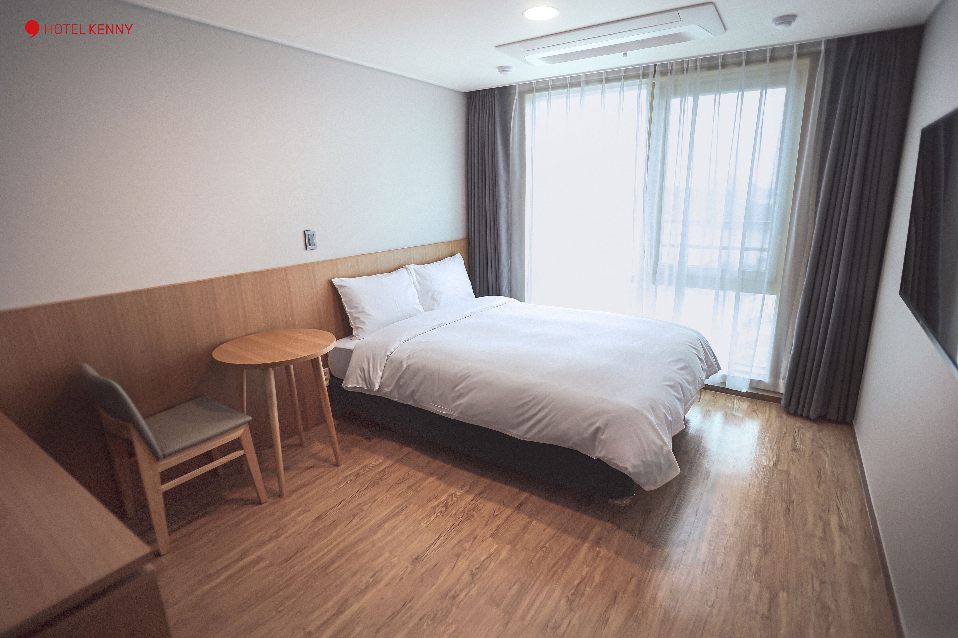 A hotel room with a bed, a small round table, a chair, and a window with curtains.