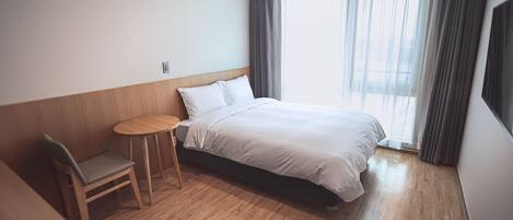 A hotel room with a bed, a small round table, a chair, and a window with curtains.