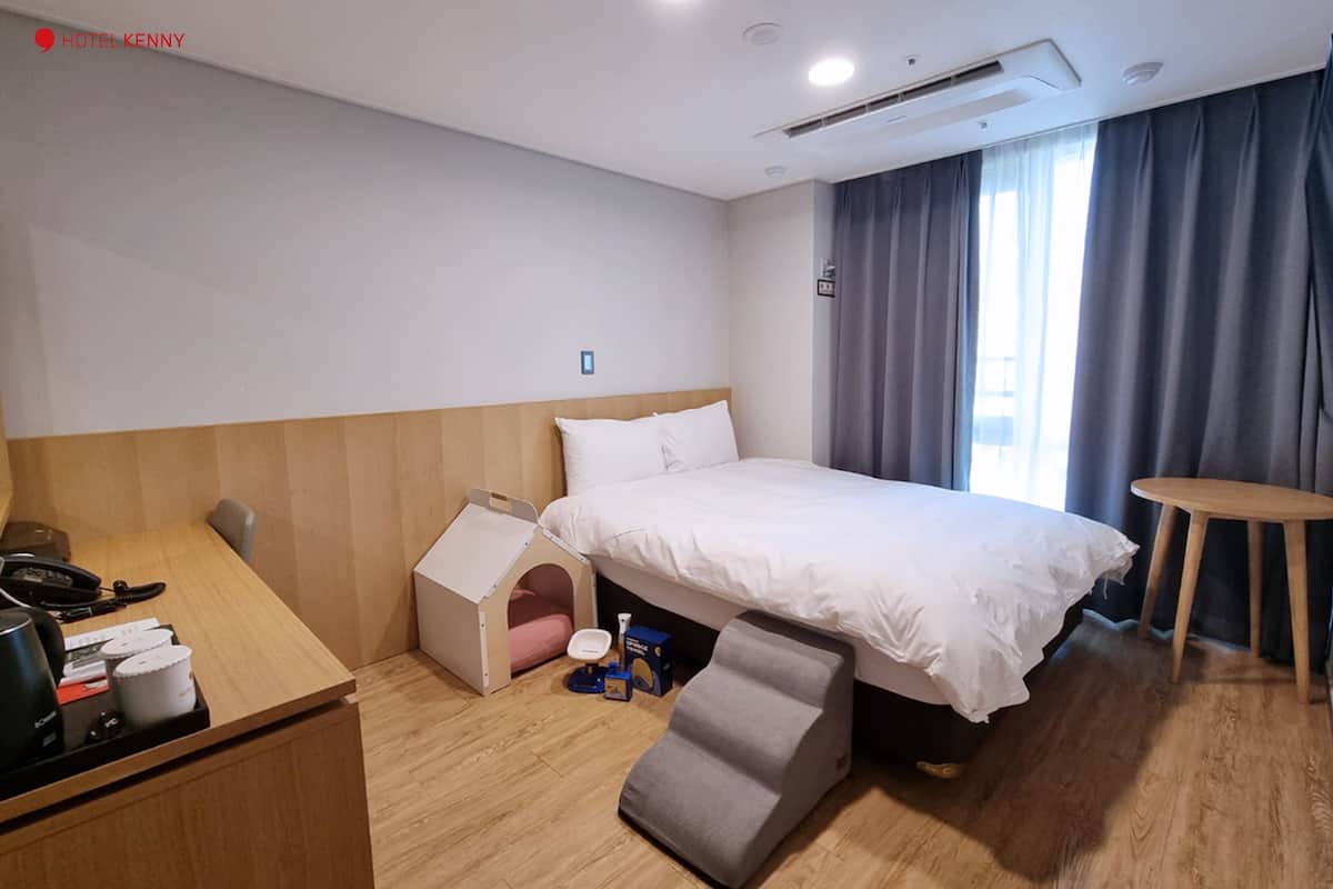 Quarto de hotel com uma cama, uma escrivaninha, um pequeno parquinho e uma mesa de cabeceira.
