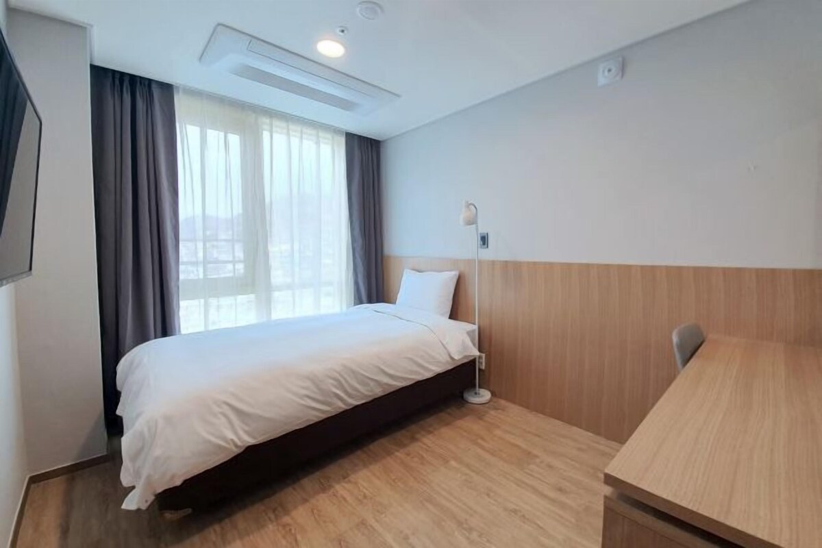 A hotel room with a bed, a desk, a lamp, and a window with curtains.