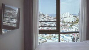 A hotel room with a large window offering a view of a densely packed urban area with various buildings and a mountain in the distance. - Hotel Kenny Yeosu (Yeosu)