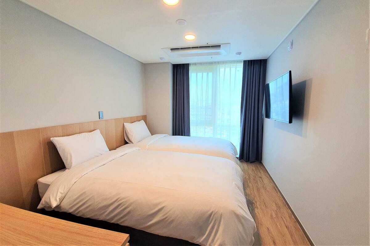 Quarto de hotel com duas camas, televisão de tela plana na parede e janela com cortinas.