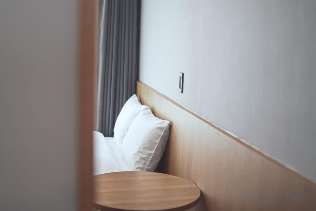 A corner of a room with a wooden headboard, a round wooden table, and a grey curtain.