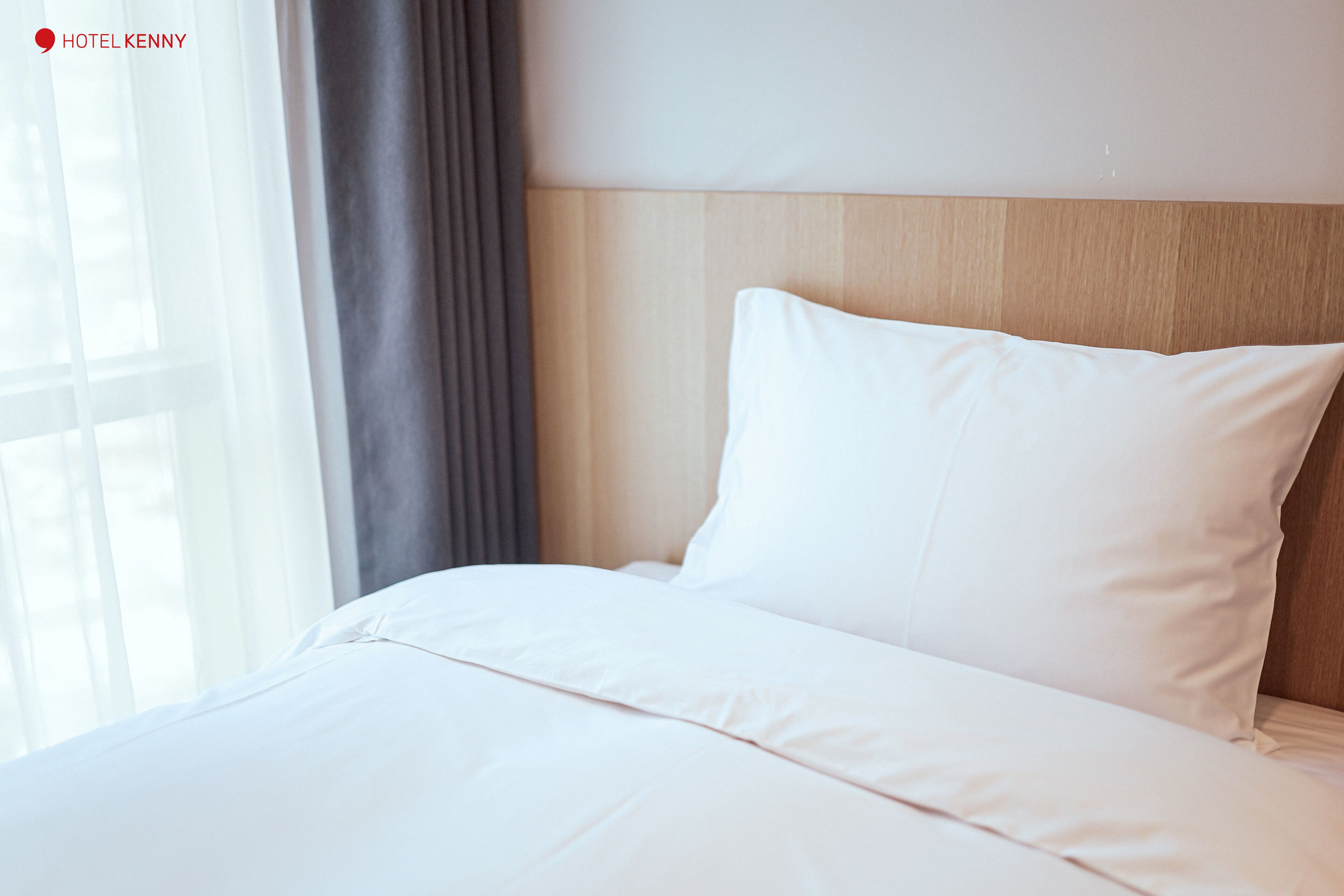A hotel room with a neatly made bed, a wooden headboard, and a window with curtains.
