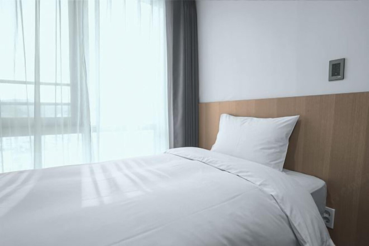 A hotel room with a large bed, a wooden headboard, and a window with sheer curtains.