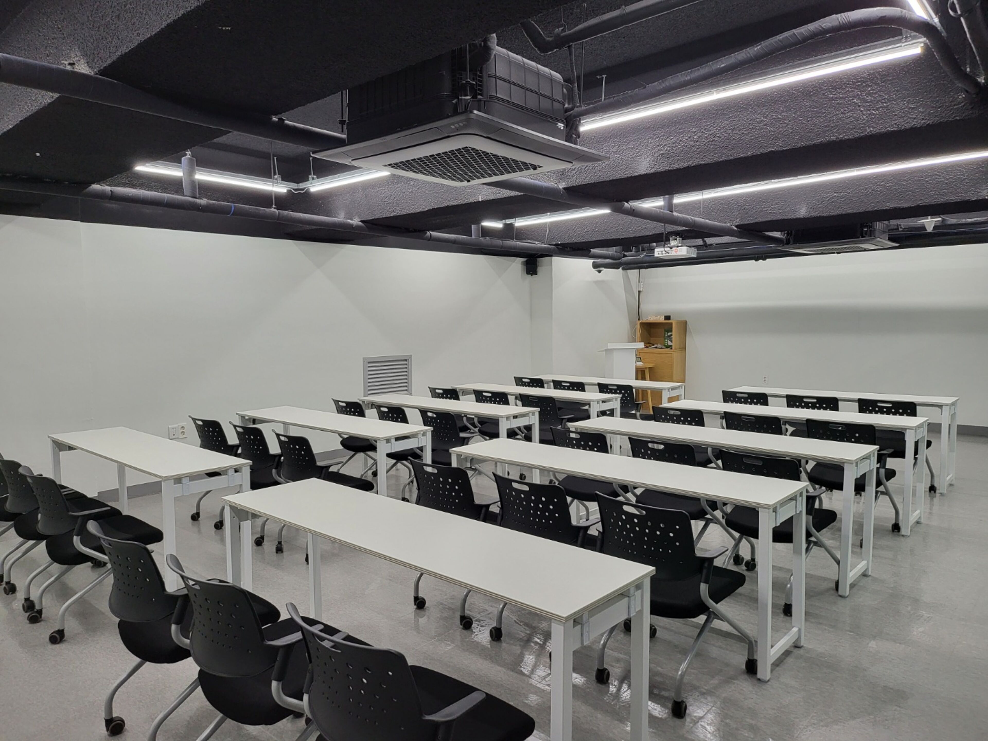 A conference room with multiple tables and chairs, a projector screen, and a whiteboard.