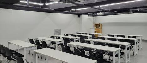A conference room with multiple tables and chairs, a projector screen, and a whiteboard.