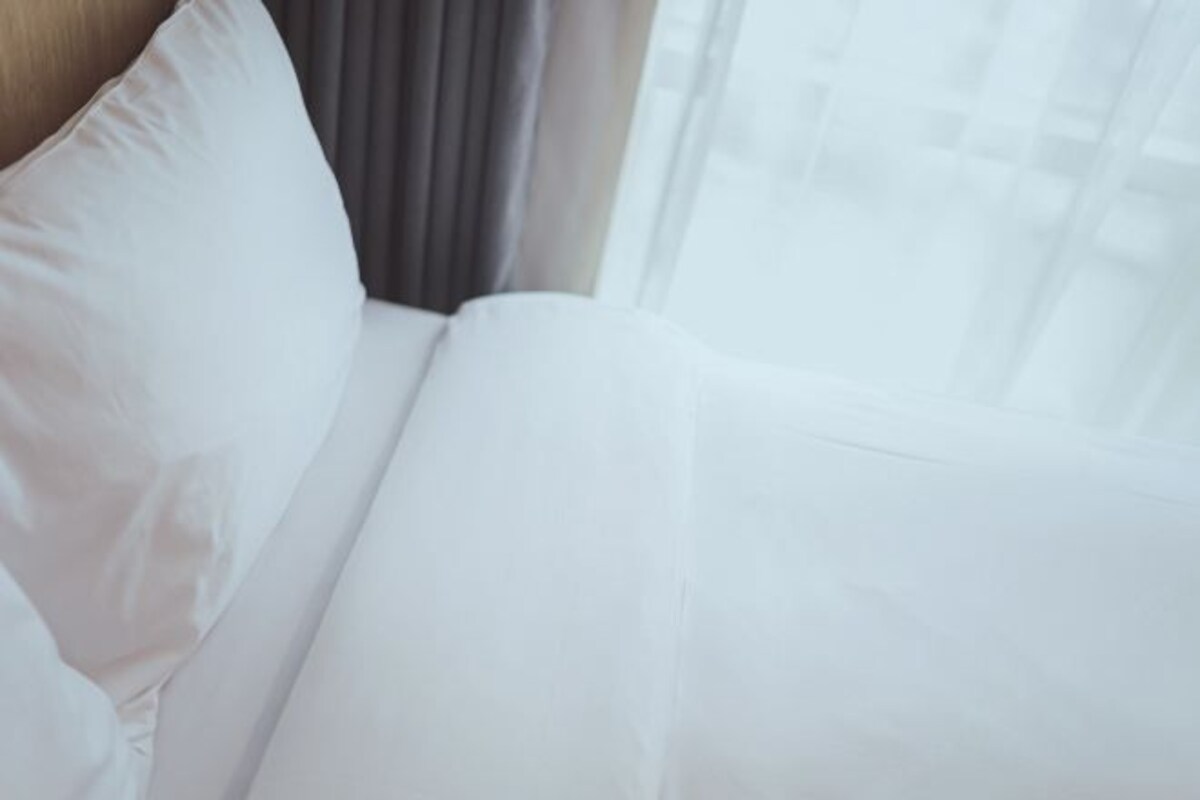 A white bed with a grey headboard and a window with sheer curtains.