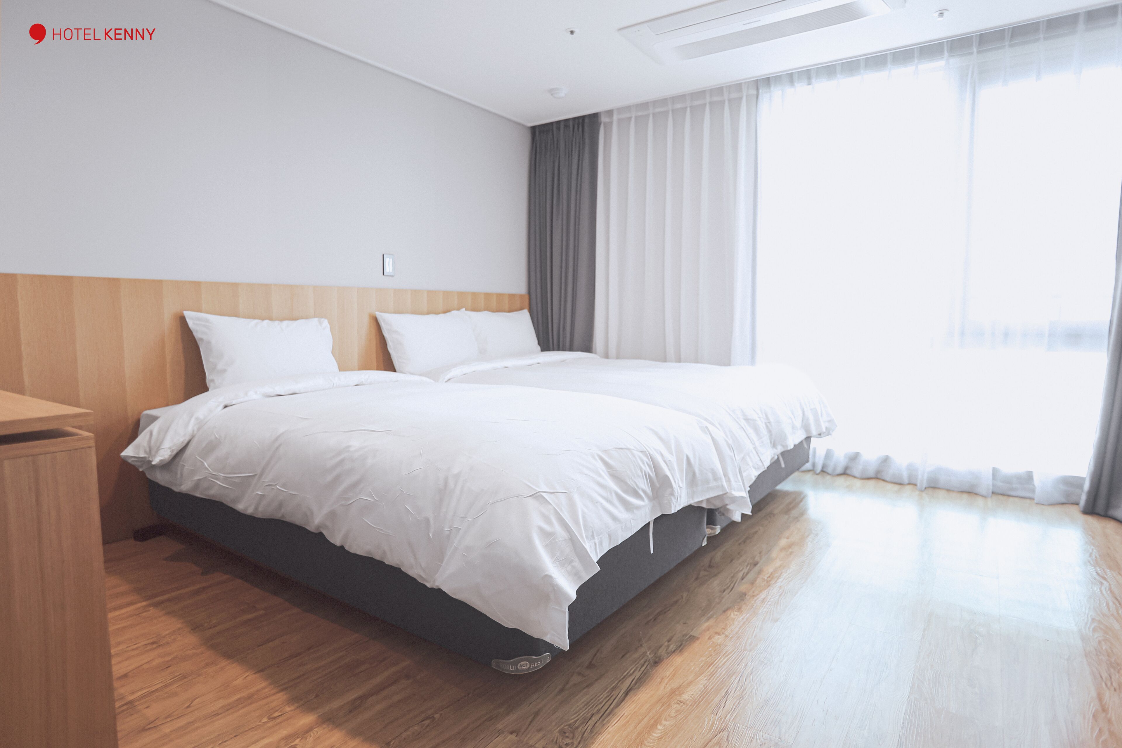 A hotel room with a large bed, a wooden nightstand, and a large window with curtains.