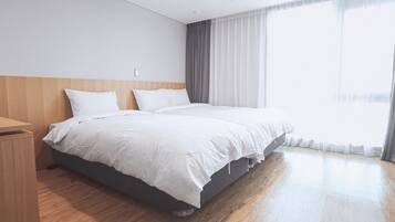 A hotel room with a large bed, a wooden nightstand, and a large window with curtains.
