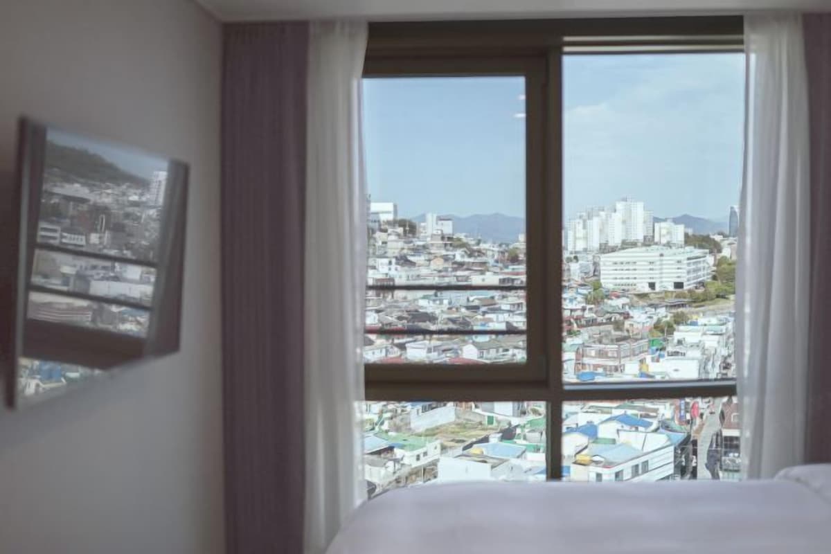 A hotel room with a large window offering a city view.
