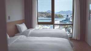 A hotel room with a large window offering a view of a cityscape and mountains. - Hotel Kenny Yeosu (Yeosu)