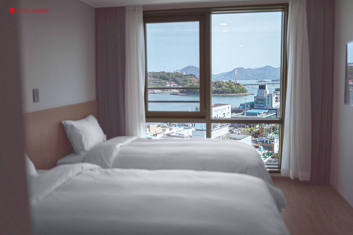 Quarto de hotel com uma janela ampla que oferece vista para a paisagem urbana e montanhas.