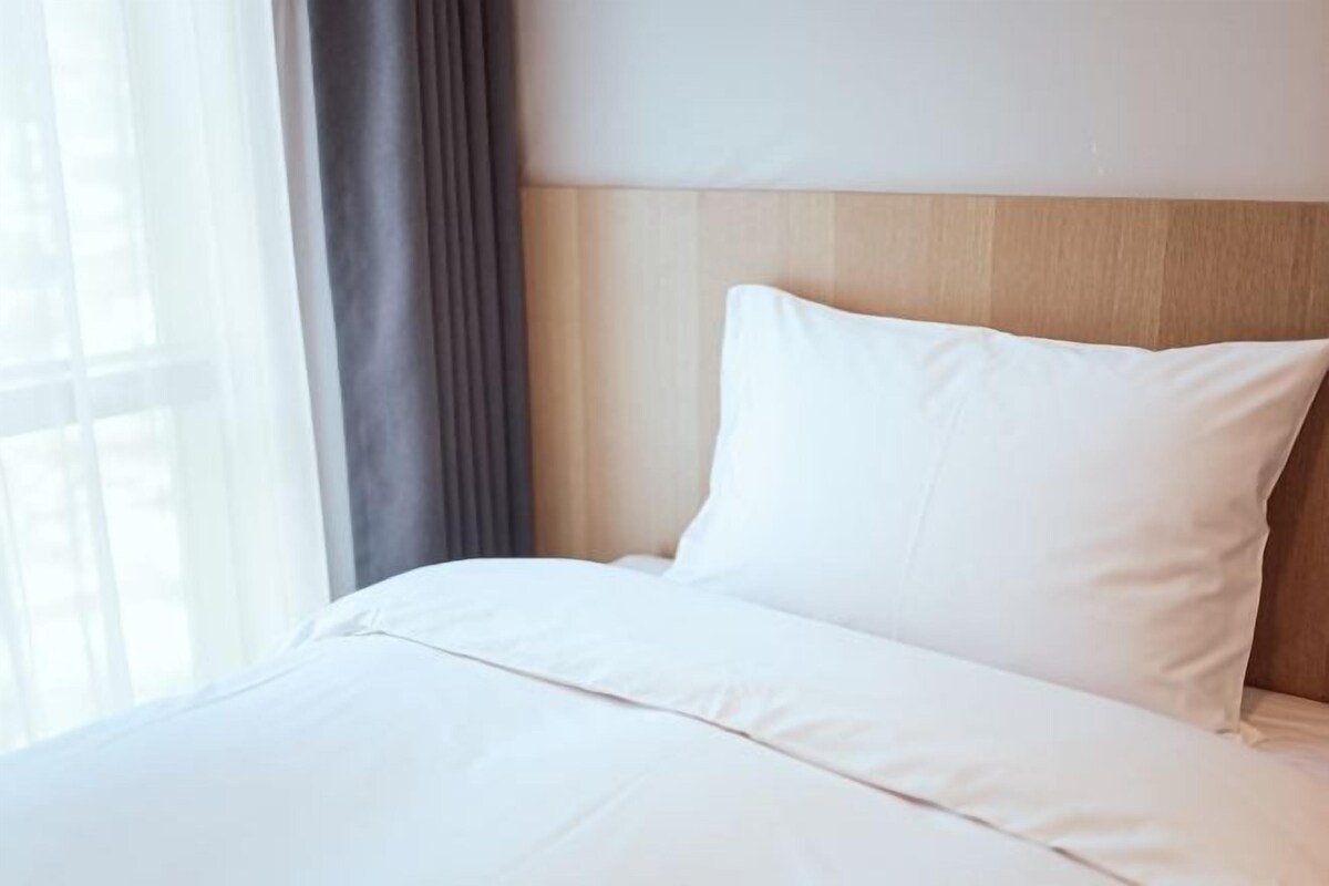 Habitación de hotel con cabecera de madera, ropa de cama blanca y una ventana con cortinas.