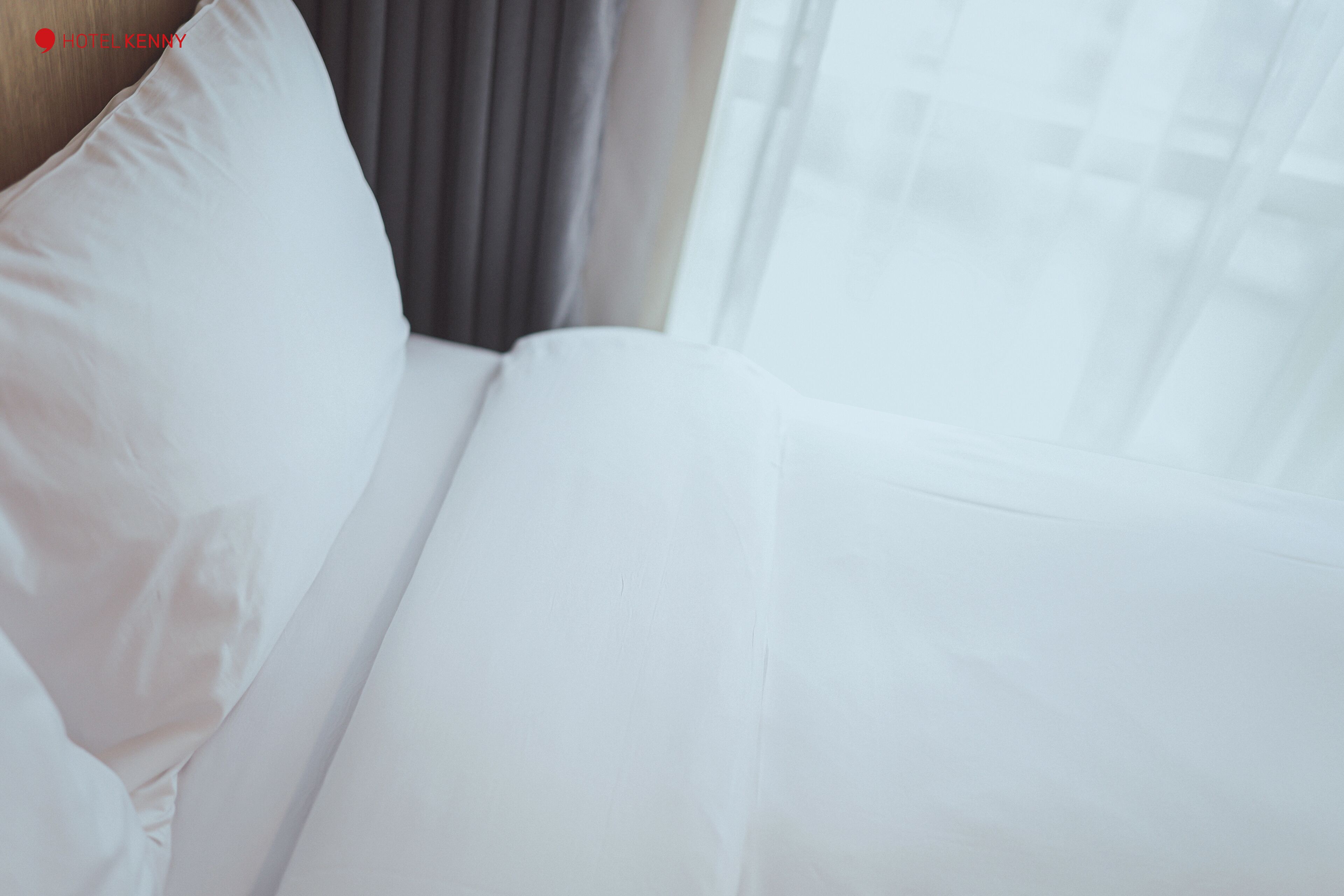 A white bed with a pillow and a window with curtains.
