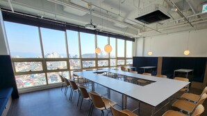A spacious conference room with a large table and chairs, large windows offering a city view, and modern pendant lighting. - Hotel Kenny Yeosu (Yeosu)