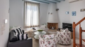Una sala de estar con un sofá, un sillón y una pequeña mesa de centro. Hay una chimenea, un televisor y una escalera.