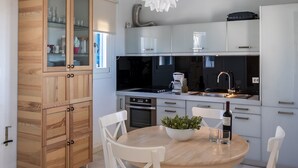 Una cocina moderna con armarios blancos, un mueble de madera con puertas de cristal, una mesa redonda de comedor con sillas blancas y un techo con vigas a la vista.