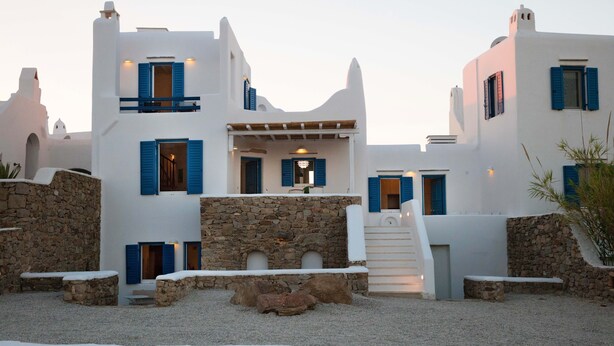 Un edificio blanco con contraventanas azules, paredes de piedra y un patio de grava.