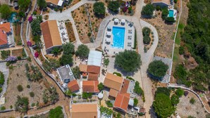 An aerial view of a residential area with multiple houses, a central swimming pool, and surrounding greenery.