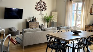 A modern living room with a sofa, dining table, chairs, a TV, and a decorative tree wall piece.