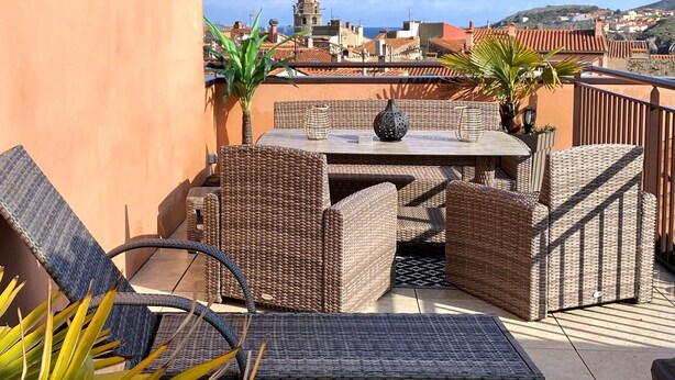 A rooftop terrace with wicker furniture, a table, and potted plants.