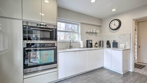 A modern kitchen with built-in appliances, a large window, and a clock on the wall. - Home w/ Office + Yard: 25 Mi to Downtown Chicago! (Glen Ellyn)