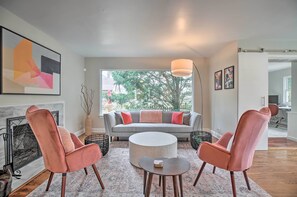 Un salon moderne avec un canapé gris, deux fauteuils roses, une table basse ronde et une cheminée.