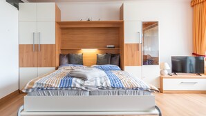 Ein modernes Schlafzimmer mit Bett, Holz-Kopfteil, integriertem Kleiderschrank, Nachttisch und Fernseher.