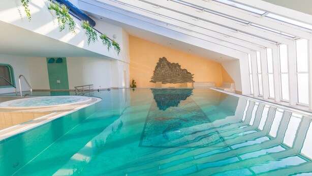Ein großer, überdachter Pool mit klarem Wasser, eine Whirlwanne und eine dekorative Steinwand.