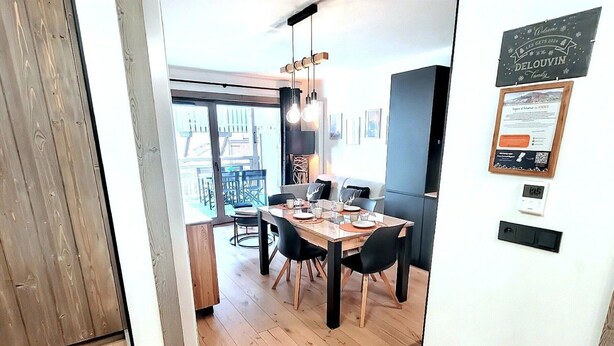 A dining area with a wooden table and chairs, a hanging light fixture, and a view of the outdoors. - Flat for 4, central Les Gets, WiFi, parking (Les Gets)