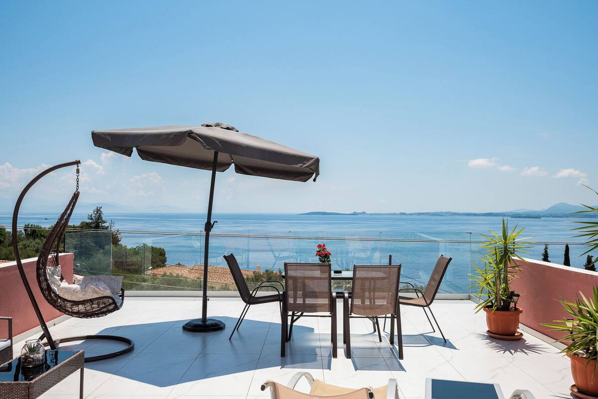 A terrace with a table, chairs, an umbrella, and potted plants.