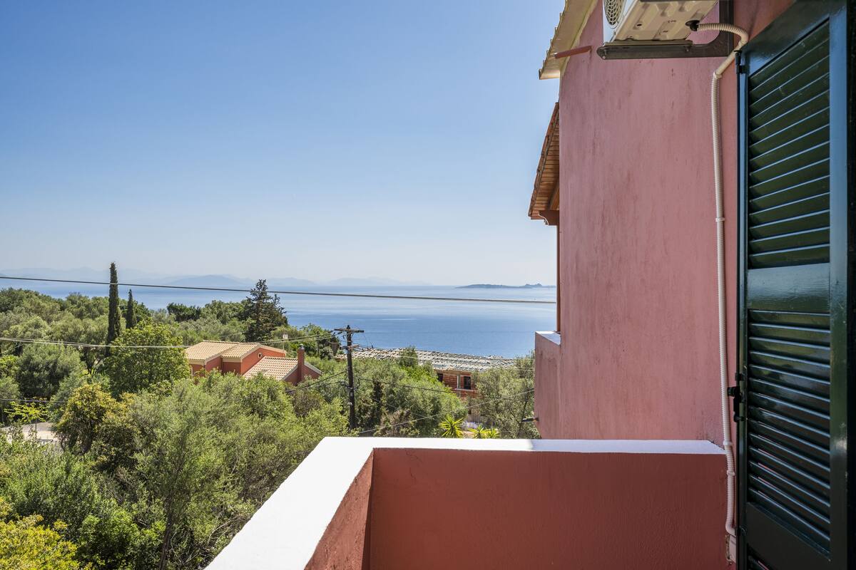A balcony with a view of a coastal landscape, including a body of water and distant mountains.