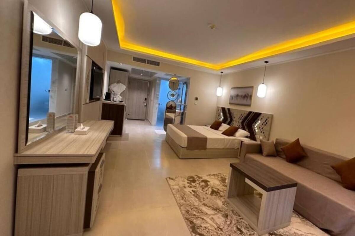 A modern hotel room with a bed, a sofa, a small table, and a mirror.