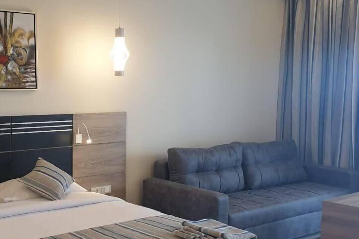 A hotel room with a bed, a sofa, a small table, and a painting on the wall.