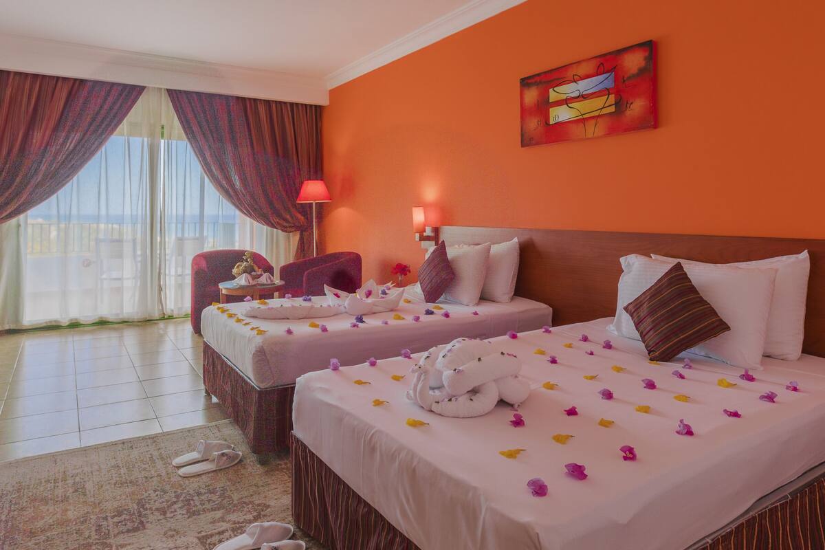 A hotel room with two beds, a sitting area with a chair, a table, and a view of the outdoors.