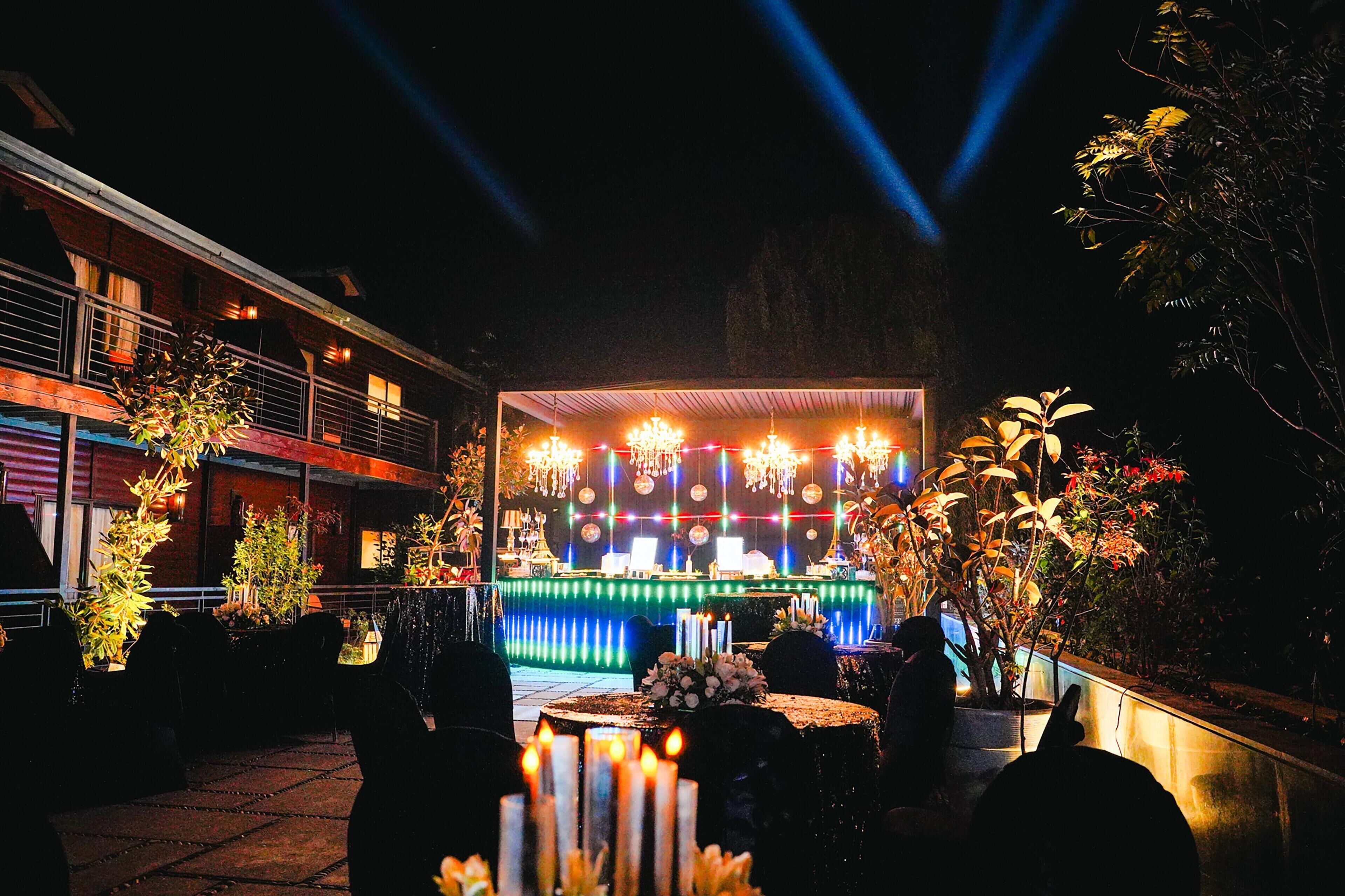 An outdoor dining area with a stage, tables, chairs, and plants.